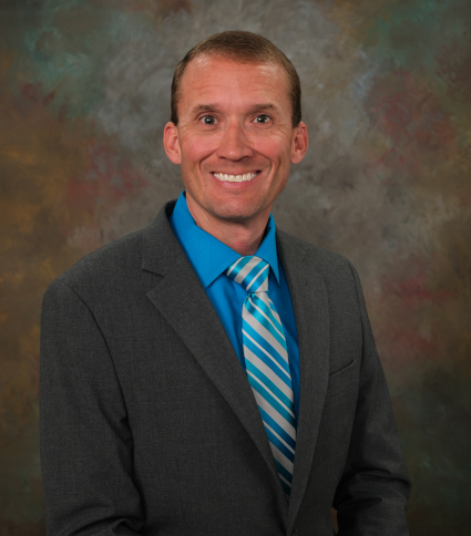 Council President Chad Leverett is wearing a gray jacket, blue shirt, and blue and yellow tie.